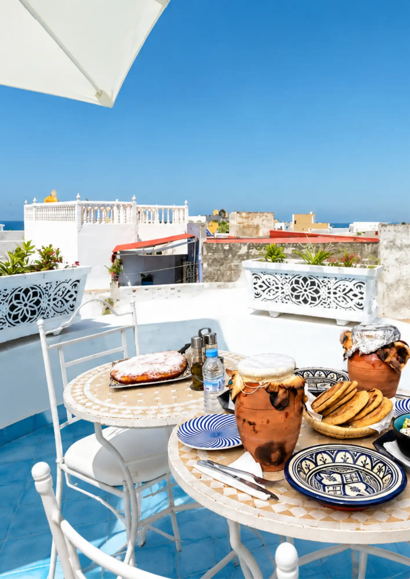 Rooftop terrace with tanjia clay pots and Moroccan food spread rooftop dining after a cooking class in Asilah with whitewashed medina views